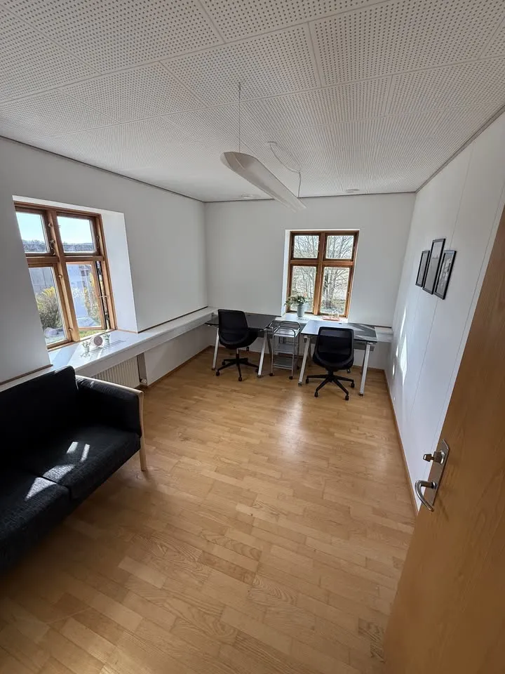 Kontorlokale på Hundtofte 14A med to skriveborde under vinduer til to sider, sofa, trægulv og akustikloft